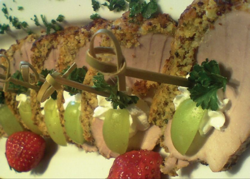 Aufgeschnittener Braten mit Kräuterkruste, garniert mit Trauben am Spieß und Erdbeeren