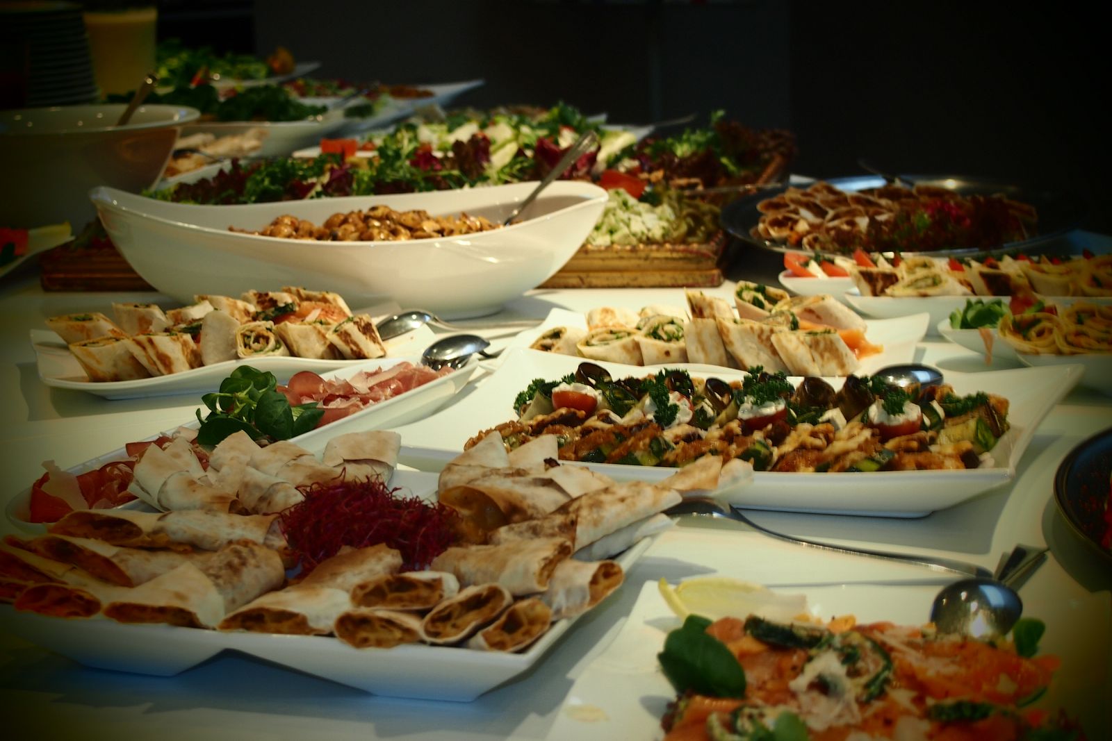 Buffet mit Wraps, Salatschalen und Platten in warmem Licht