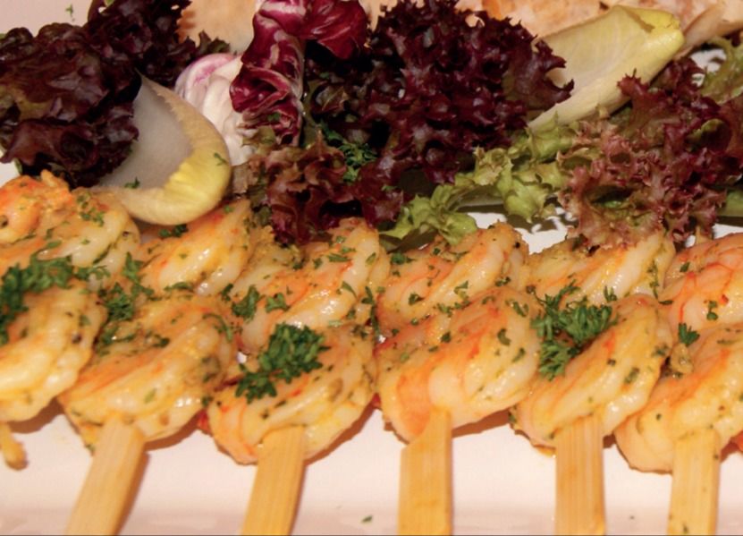 Garnelenspieße in einer Reihe, dahinter Salatblätter