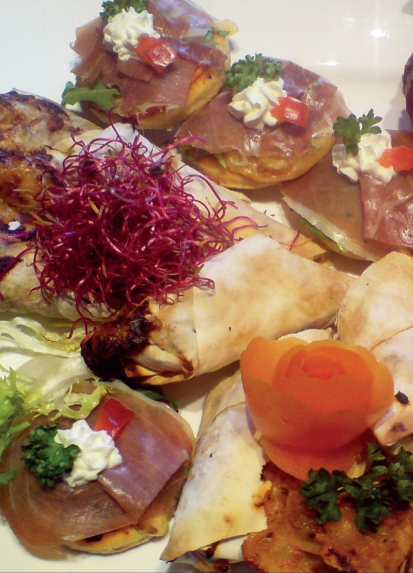 Kanapees mit Schinken und Frischkäsetupfen, daneben Wraps und eine Tomatenrose