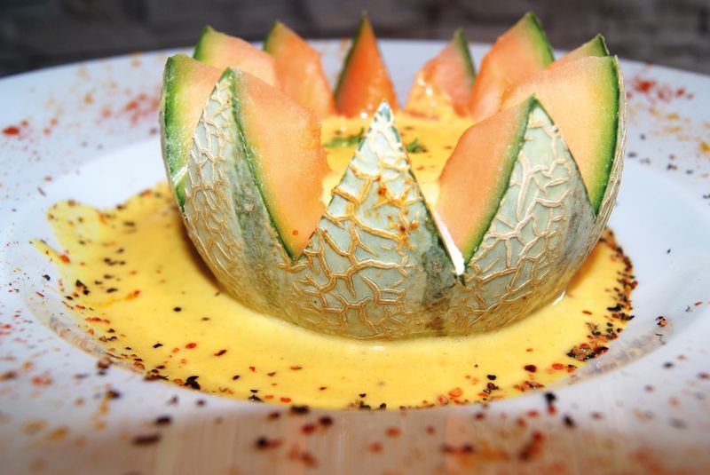 Melone mit gezacktem Rand in einer gelben Suppe mit buntem Pfeffer